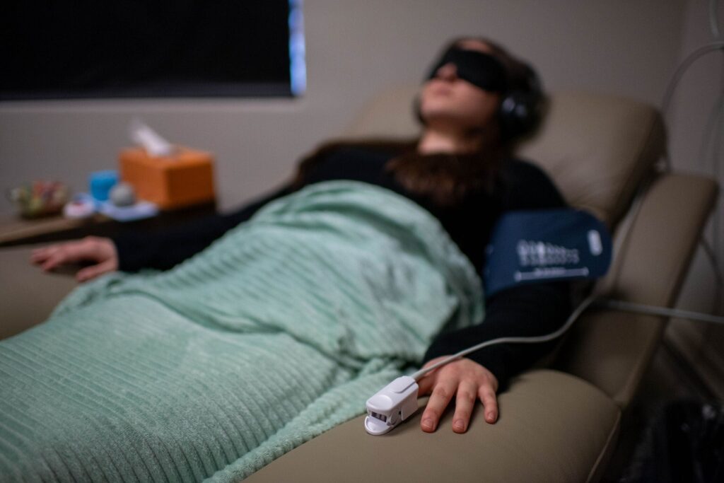 A patient wearing a eye mask rests comfortably during a monitored ketamine therapy infusion session.