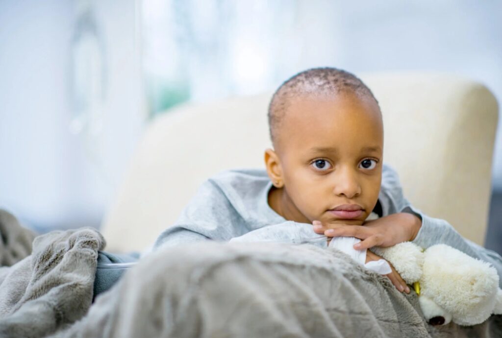 Smiling young girl wearing a blue headscarf and holding a stuffed bunny, symbolizing courage in child cancer survivorship.