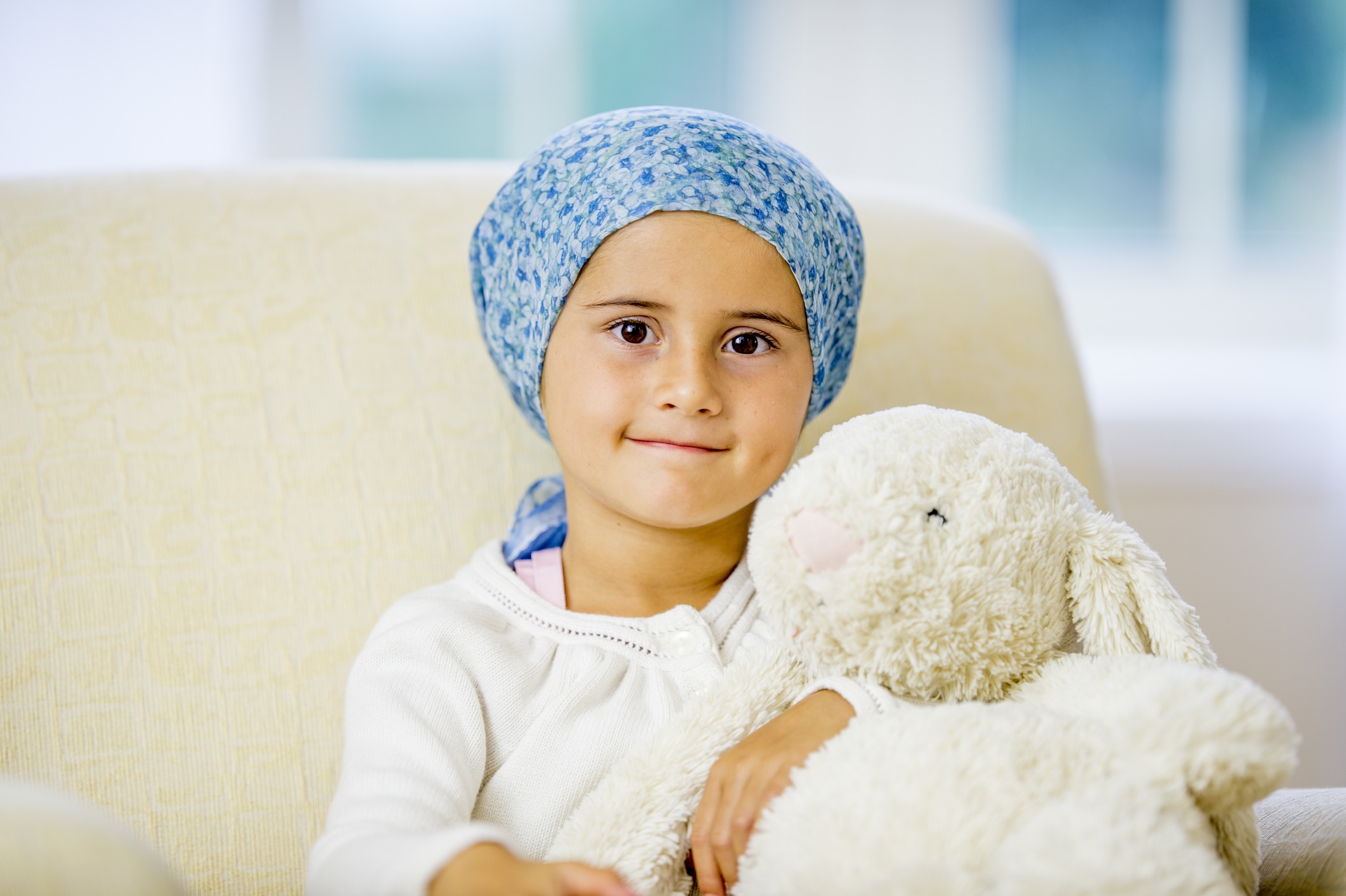 Young child resting comfortably on a sofa with a teddy bear, highlighting resilience and hope in child cancer survivorship care.