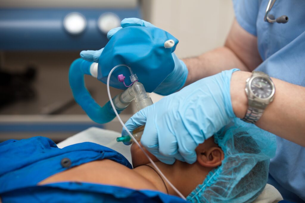 Anesthesiologist using a breathing bag and mask for a child during pediatric surgery and anesthesia care.