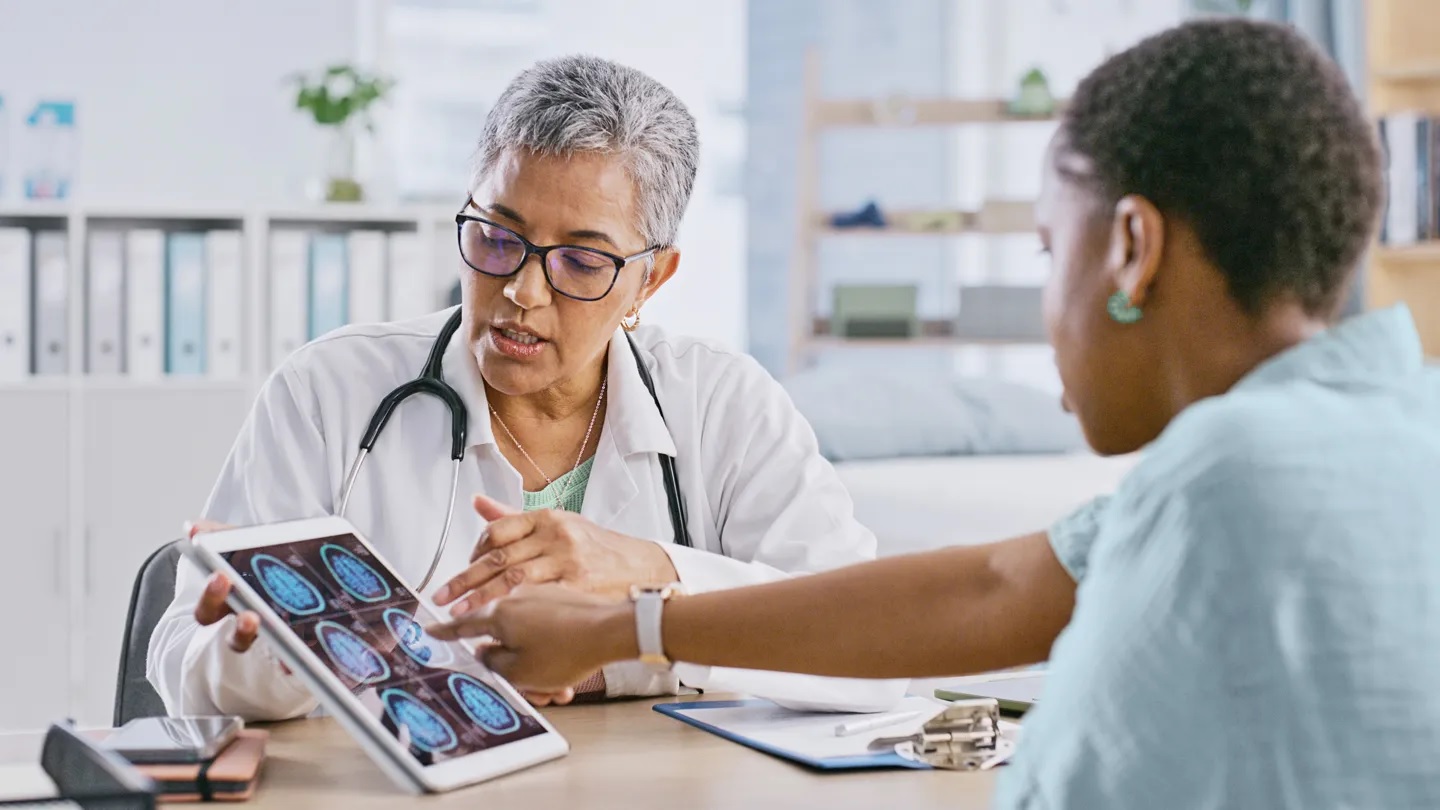A doctor wearing glasses explaining digital brain scans on a tablet to a patient as part of clinical research for CIDP