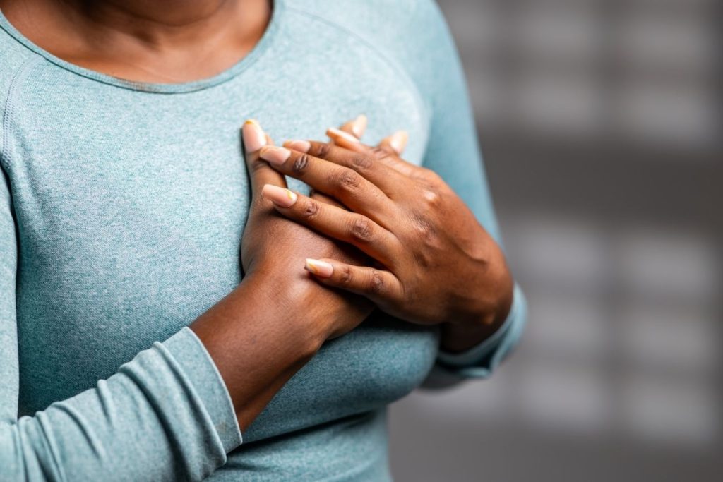 Black woman holding hands over her chest, highlighting self-awareness and holistic support in breast cancer care.