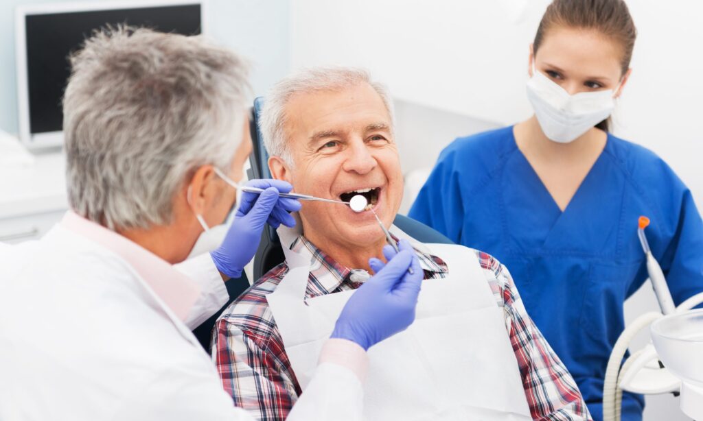 A senior male smiling, getting a dental checkup by a male dentist and a female assistant, promoting healthy teeth for life.