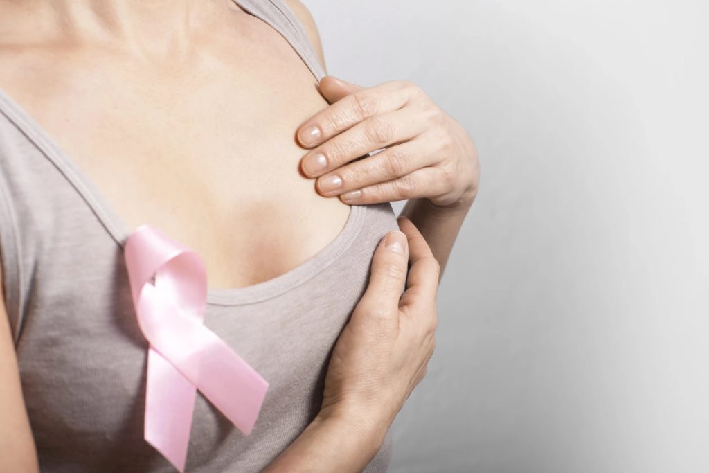A woman performing a self-exam with a pink ribbon attached, promoting breast cancer risk assessment.